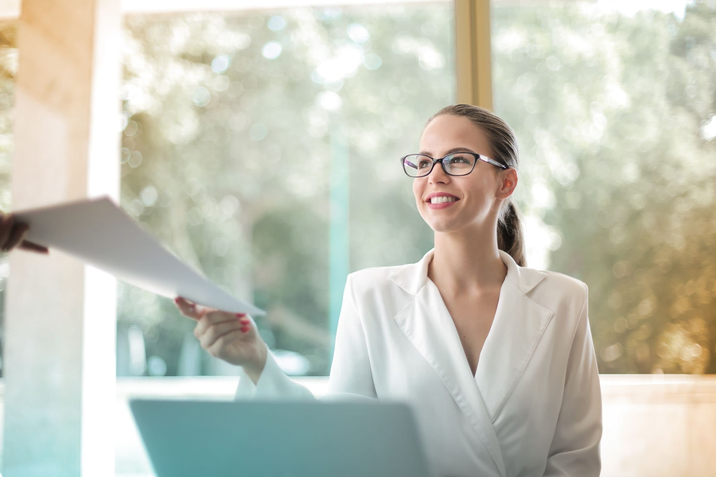 A businesswoman handing over a document at her desk, such as a certificate of insurance for a client
