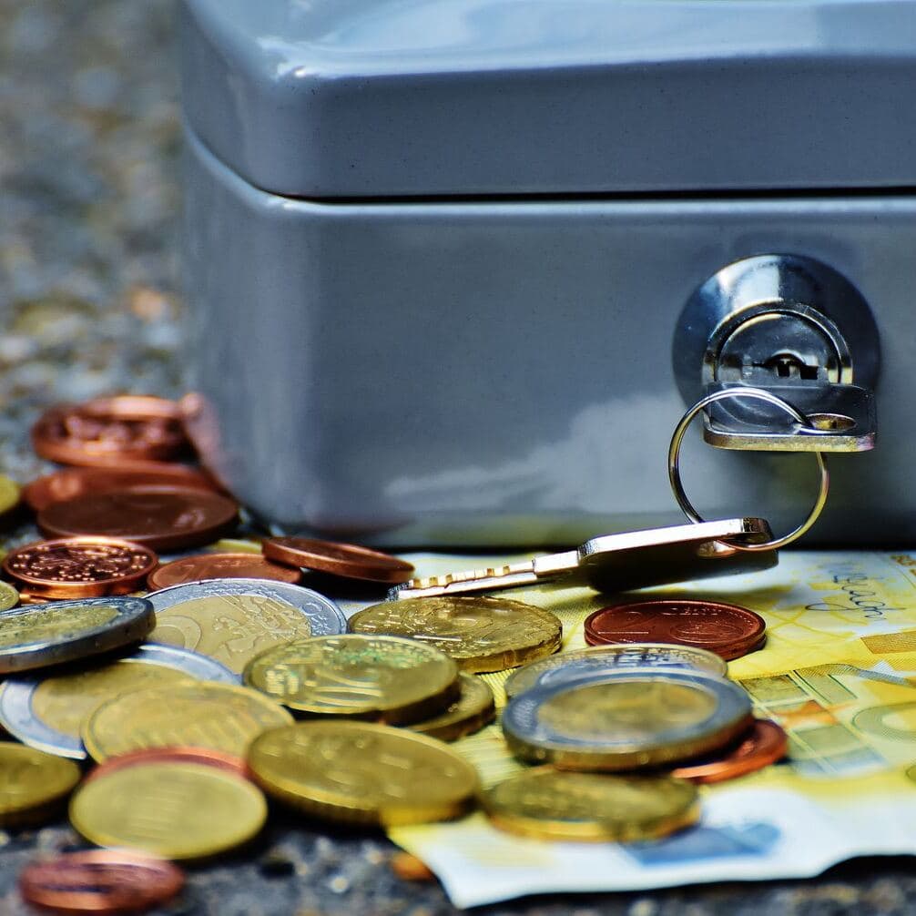 Coins and banknotes beside a locked cash box